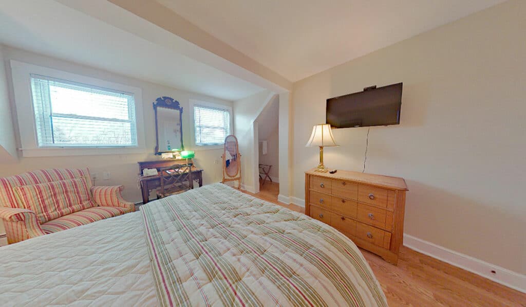 Room 213 - looking towards the foot of the bed at the tv, 3 drawer dresser with lamp, and floor mirror.